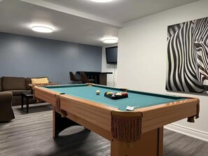A pool table with balls, a sofa, and a zebra painting on the wall. - Lakefront Adventure Cottage | Sleeps 10 | Kayaks, Dock & Hot Tub (Kawartha Lakes)