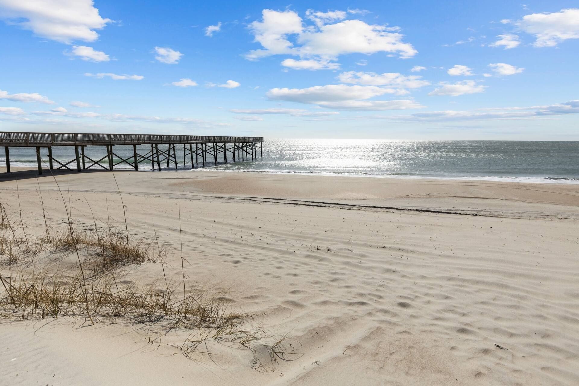 A beach with a wooden pier extending into the ocean, sandy beach, and clear sky.