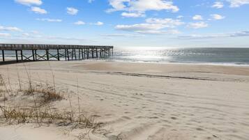 A beach with a wooden pier extending into the ocean, sandy beach, and clear sky.