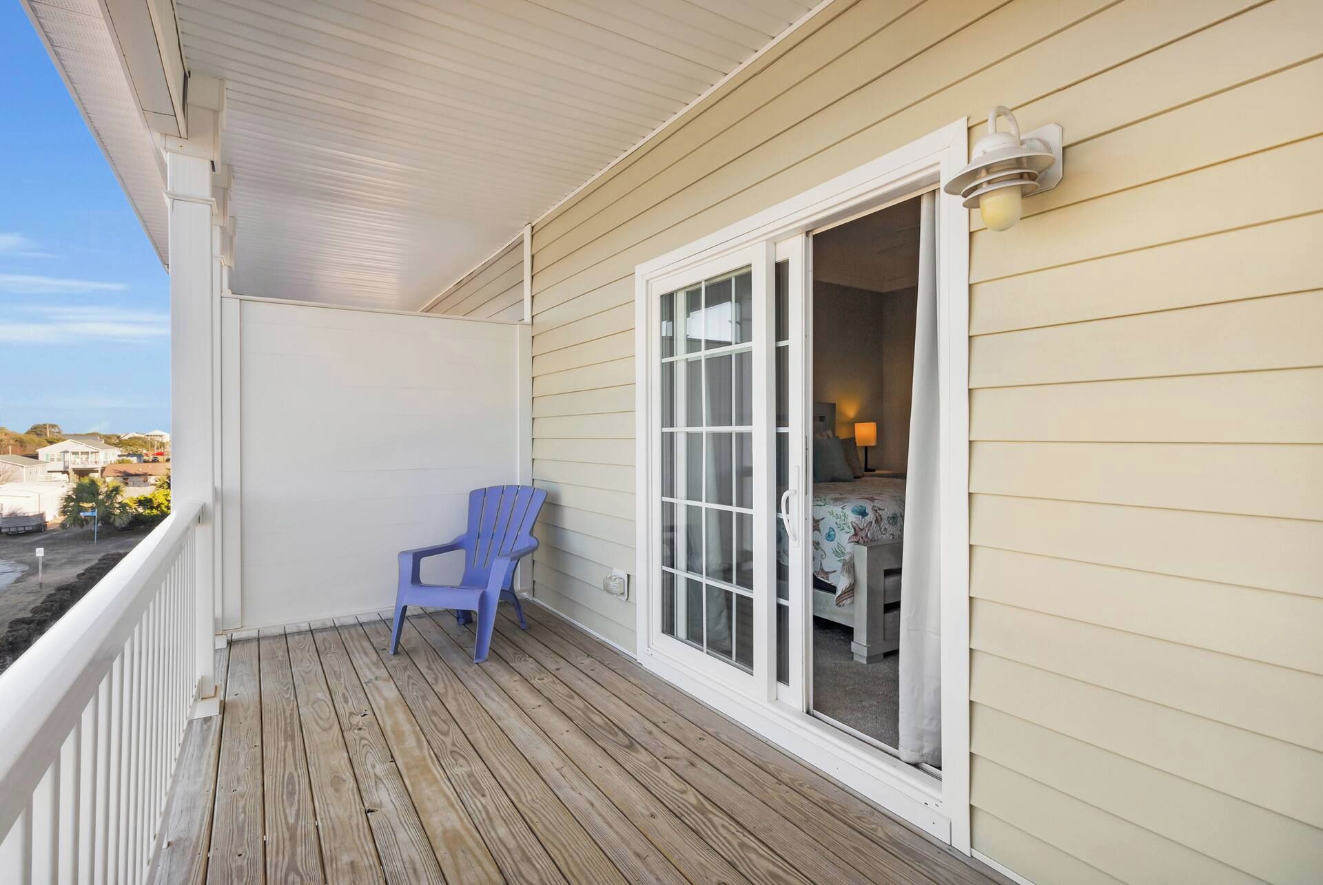 A wooden deck with a blue chair, a white-framed window, and a view of the sea.