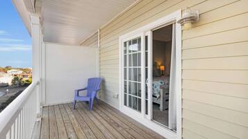 A wooden deck with a blue chair, a white-framed window, and a view of the sea.