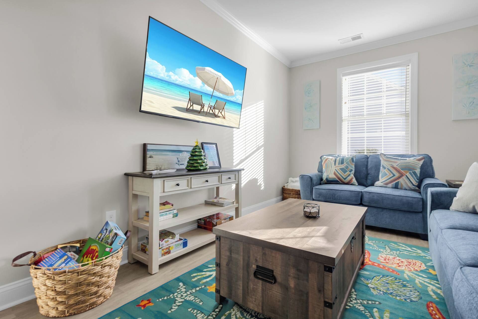A living room with a beach-themed painting, a blue sofa, a wooden coffee table, and a wicker basket.