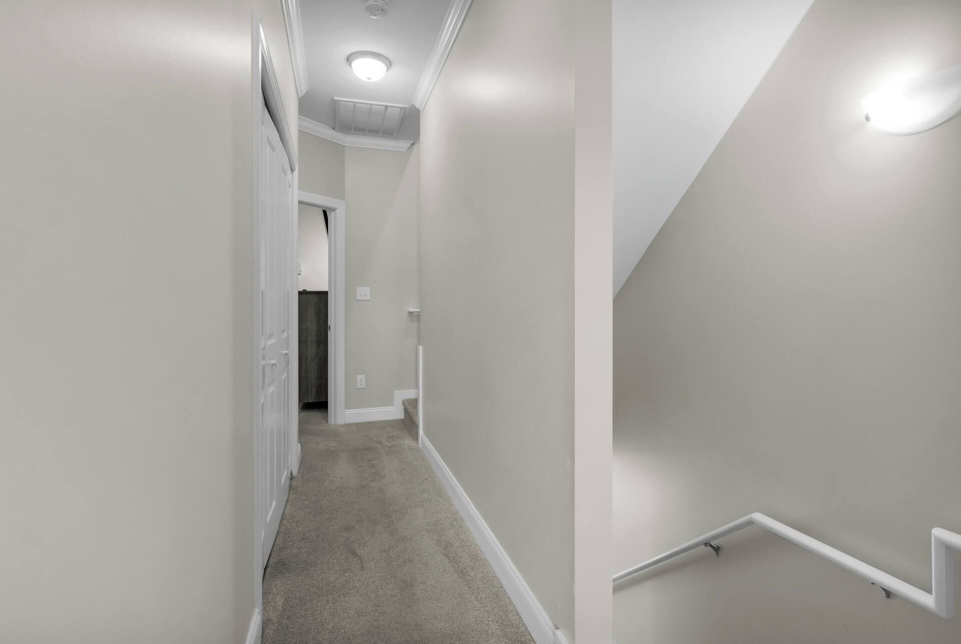 A hallway with a carpeted floor, white walls, and a white railing on the right side.