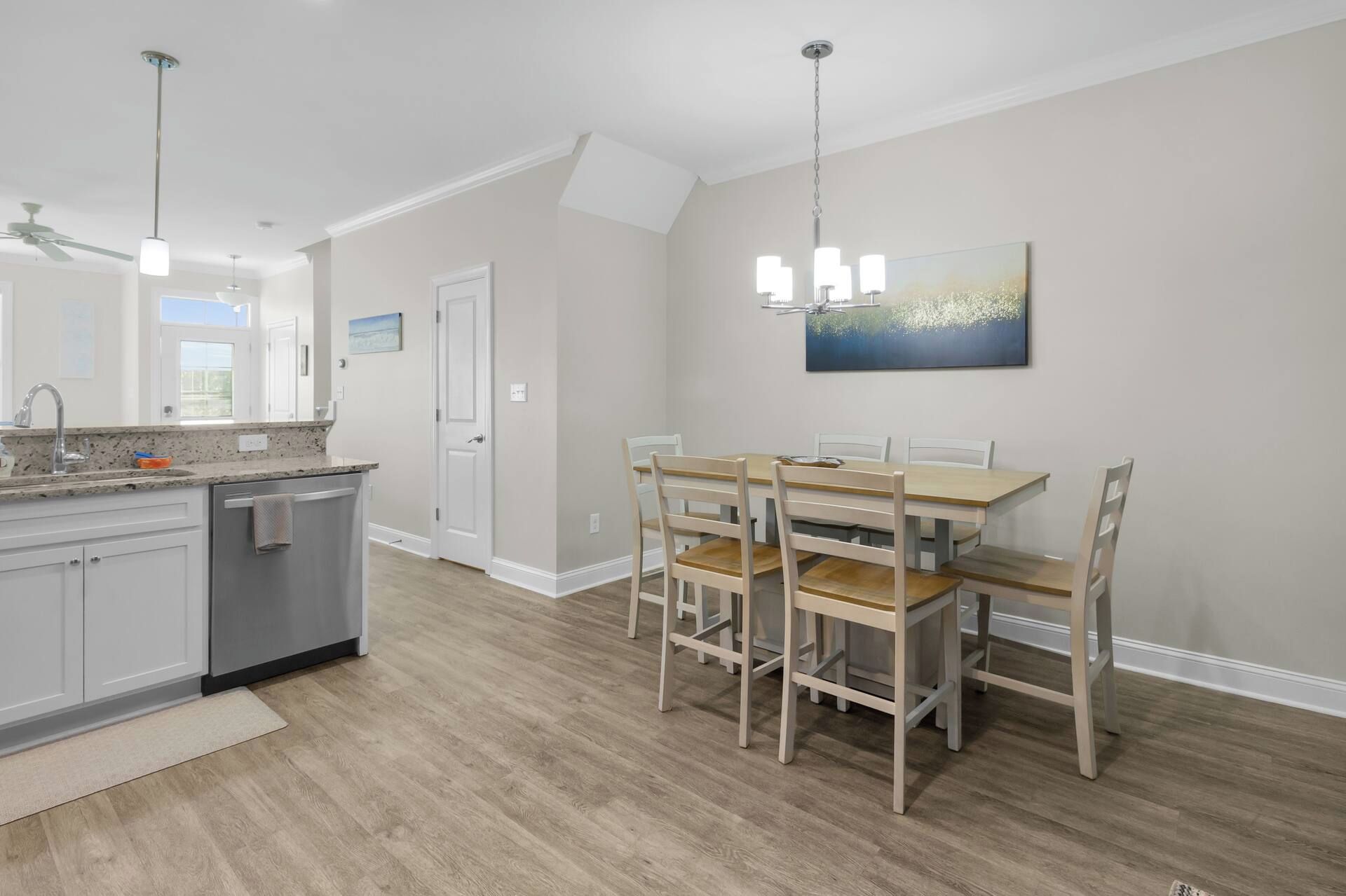 A modern kitchen with a dining area, featuring a wooden table and chairs, a painting on the wall, and a ceiling fan.