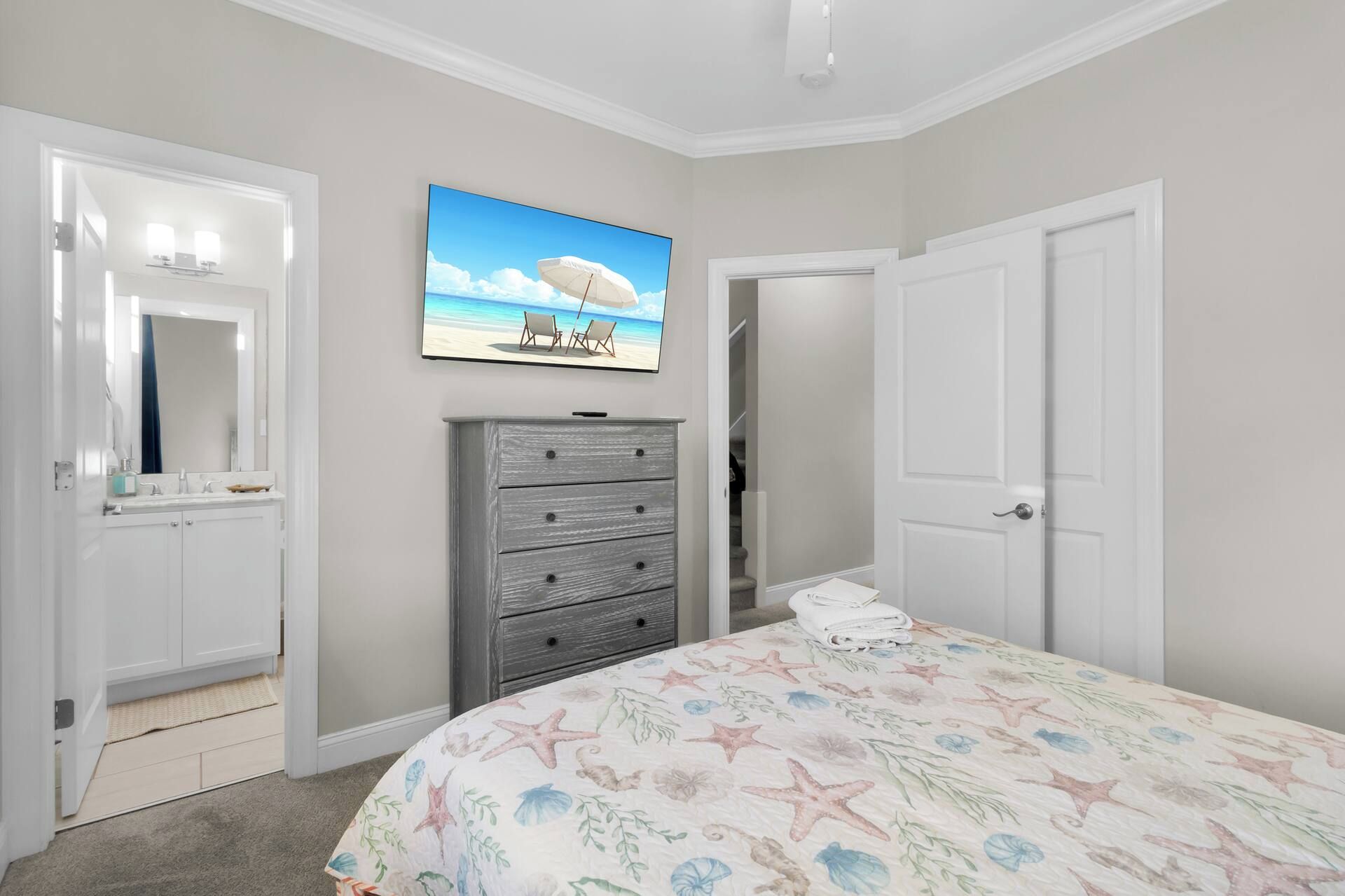 Een slaapkamer met een bed, een dressoir, een schilderij van een strand en een deur.