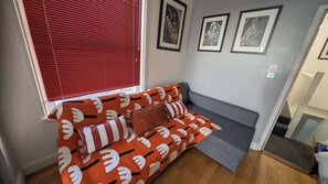 Ein Zimmer mit einer Couch an einer Wand, einem Fenster mit Jalousien und gerahmten Bildern an der Wand.