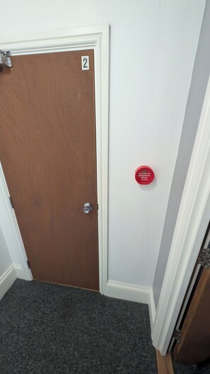A door with a number '2' on it, a red emergency glass, and a carpeted floor. - Southsea 3-Bed Flat | Spacious & Comfortable (Portsmouth)