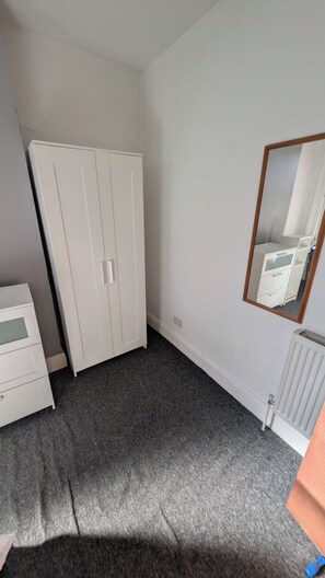 Ein Schlafzimmer mit Kleiderschrank, Schminktisch, Heizkörper und einem Spiegel an der Wand.