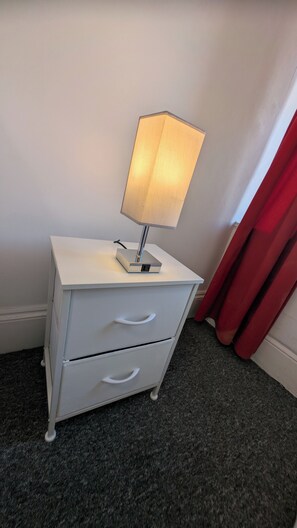 Ein weißer Nachttisch mit Lampe, zwei Schubladen und einer Steckdose.
