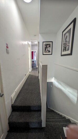 Eine Treppe mit Teppichstufen führt zu einer Empore. Darüber an der Wand hängen zwei Bilder in Rahmen.