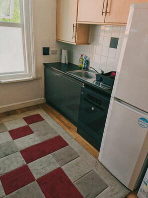Eine Küche mit einem schwarzen Herd, einem weißen Kühlschrank und einem roten und grauen Teppich.