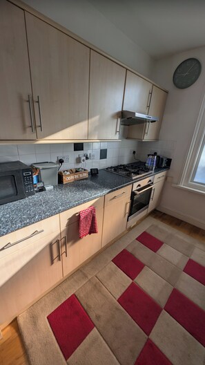 A kitchen with light wood cabinets, a gas stove, a microwave, and a coffee bar. - Southsea 3-Bed Flat | Spacious & Comfortable (Portsmouth)