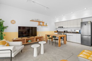 A modern living room with a flat-screen TV, a sofa, a coffee table, and a dining area with chairs.