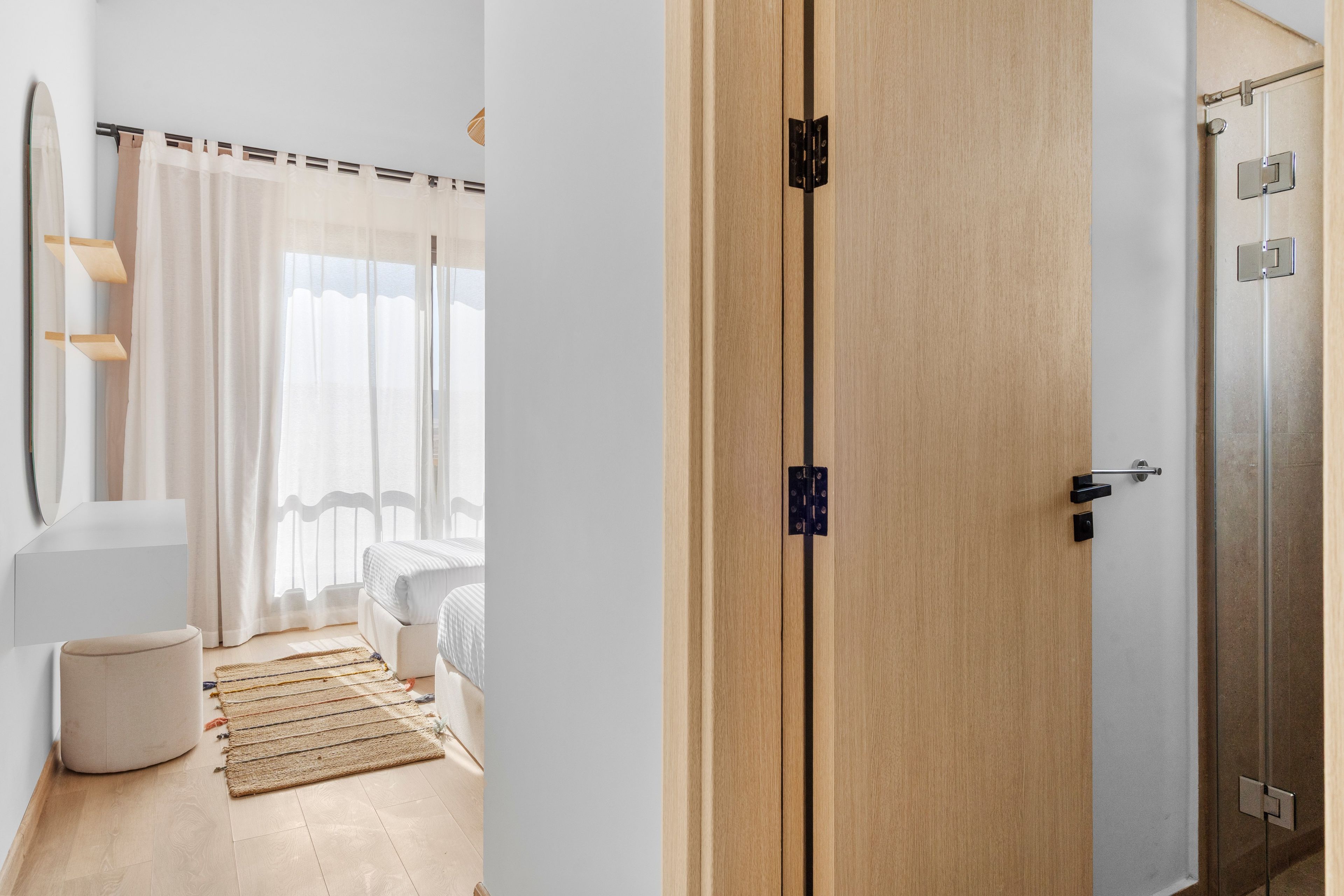 Quarto de hotel com guarda-roupa de madeira, cama com roupa de cama branca, mesa de cabeceira pequena e janela com cortinas leves.