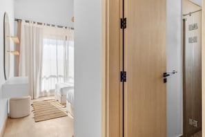Habitación de hotel con armario de madera, cama con ropa blanca, mesita de noche pequeña y ventana con cortinas traslúcidas.