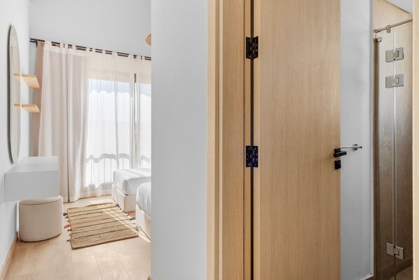 A hotel room with a wooden wardrobe, a bed with white bedding, a small bedside table, and a window with sheer curtains.