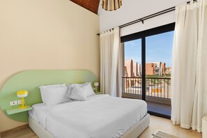 A hotel room with a bed, a nightstand, a lamp, and a view of the outside.