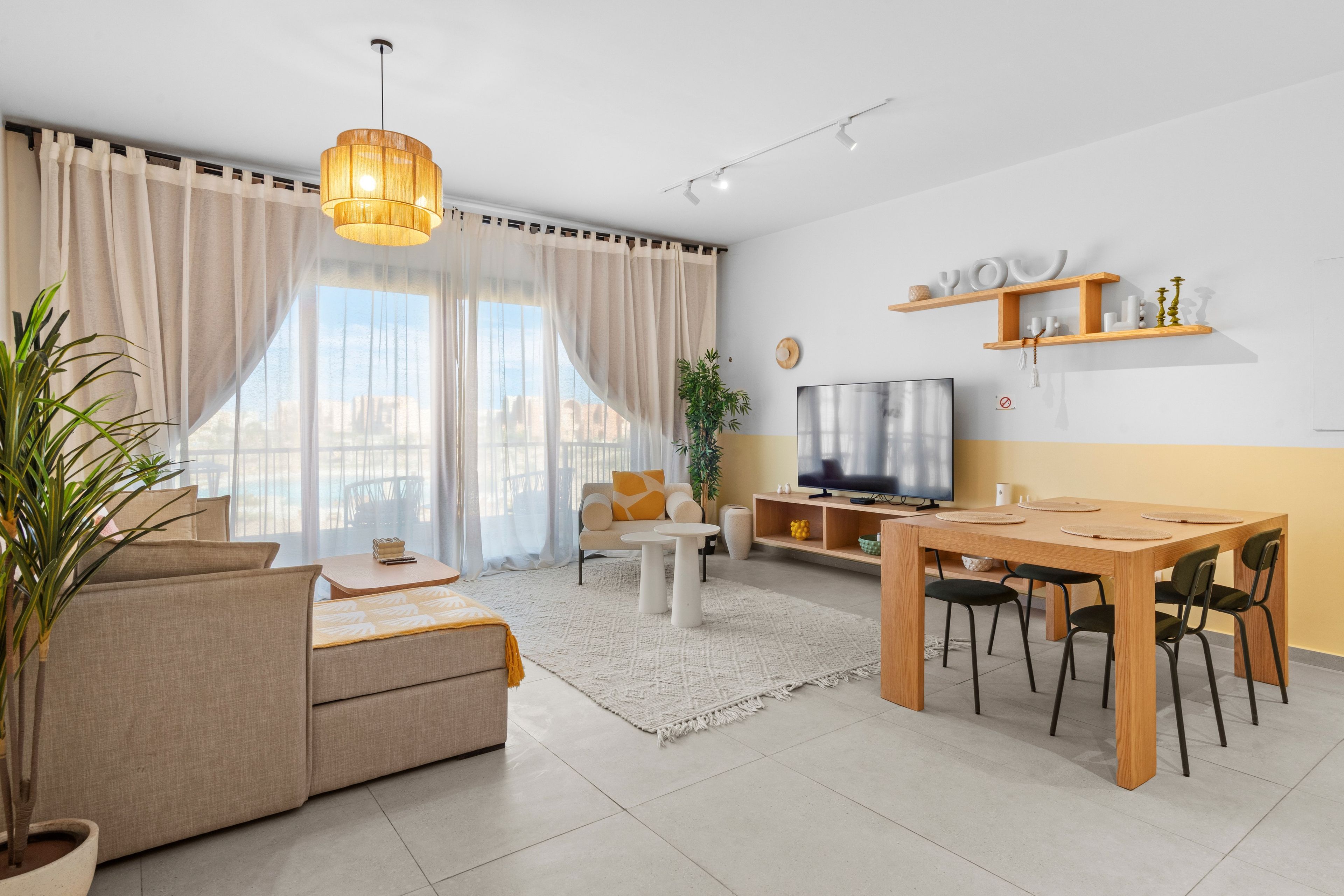 A modern living room with a sofa, coffee table, dining table, and TV.