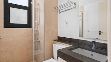 A modern bathroom with a glass shower enclosure, a white toilet, a sink with a dark countertop, and a mirror with a towel rack above it.