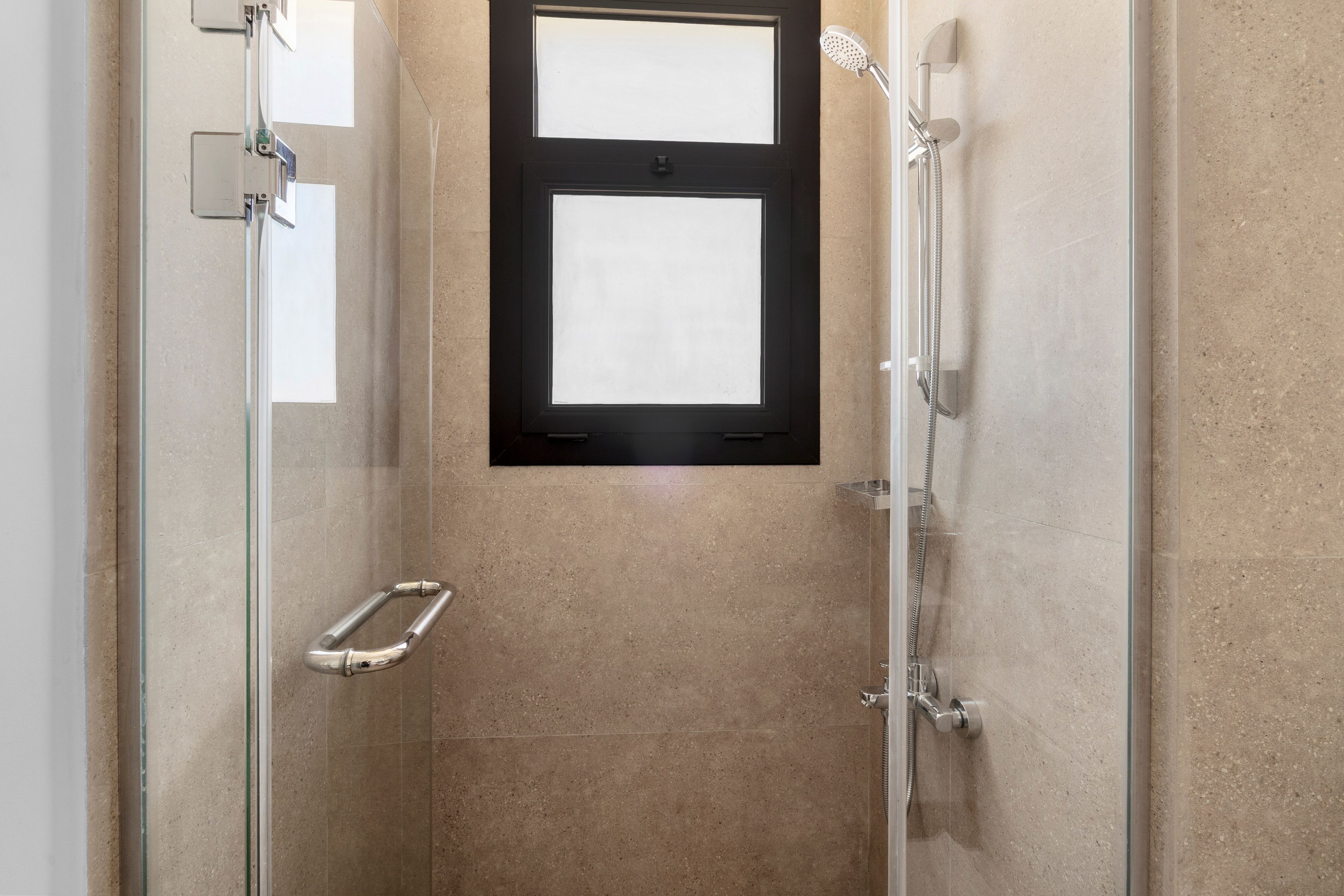 A glass-enclosed shower with a handheld showerhead and a wall-mounted faucet.