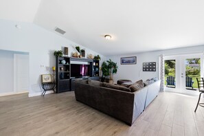 Ein modernes Wohnzimmer mit einer großen Couch, einem Fernseher und einem Essbereich mit Stühlen.