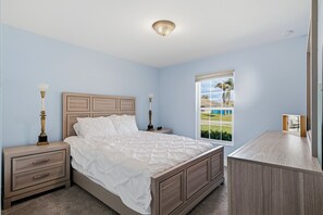 Ein Schlafzimmer mit Bett, Nachttischen, einer Kommode, einem Fenster mit Blick und einer Deckenleuchte.