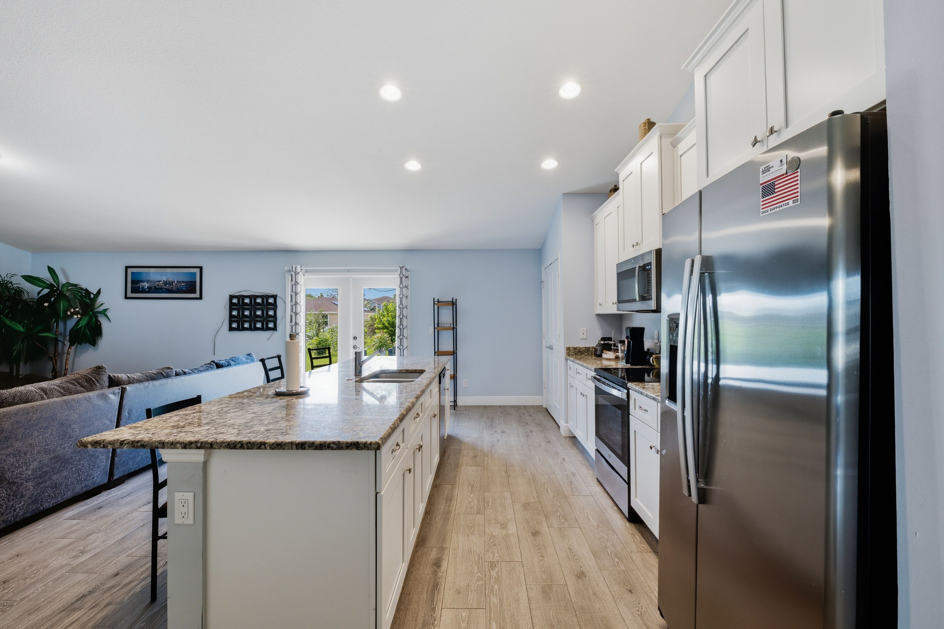 Una cocina moderna con refrigerador de acero inoxidable, armarios blancos y encimera de granito.