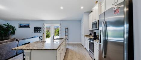 A modern kitchen with a stainless steel refrigerator, white cabinetry, and a granite countertop.