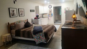 Ein Schlafzimmer mit Bett, Schreibtisch, Stuhl, Kleiderschrank und einer Küche im Hintergrund.