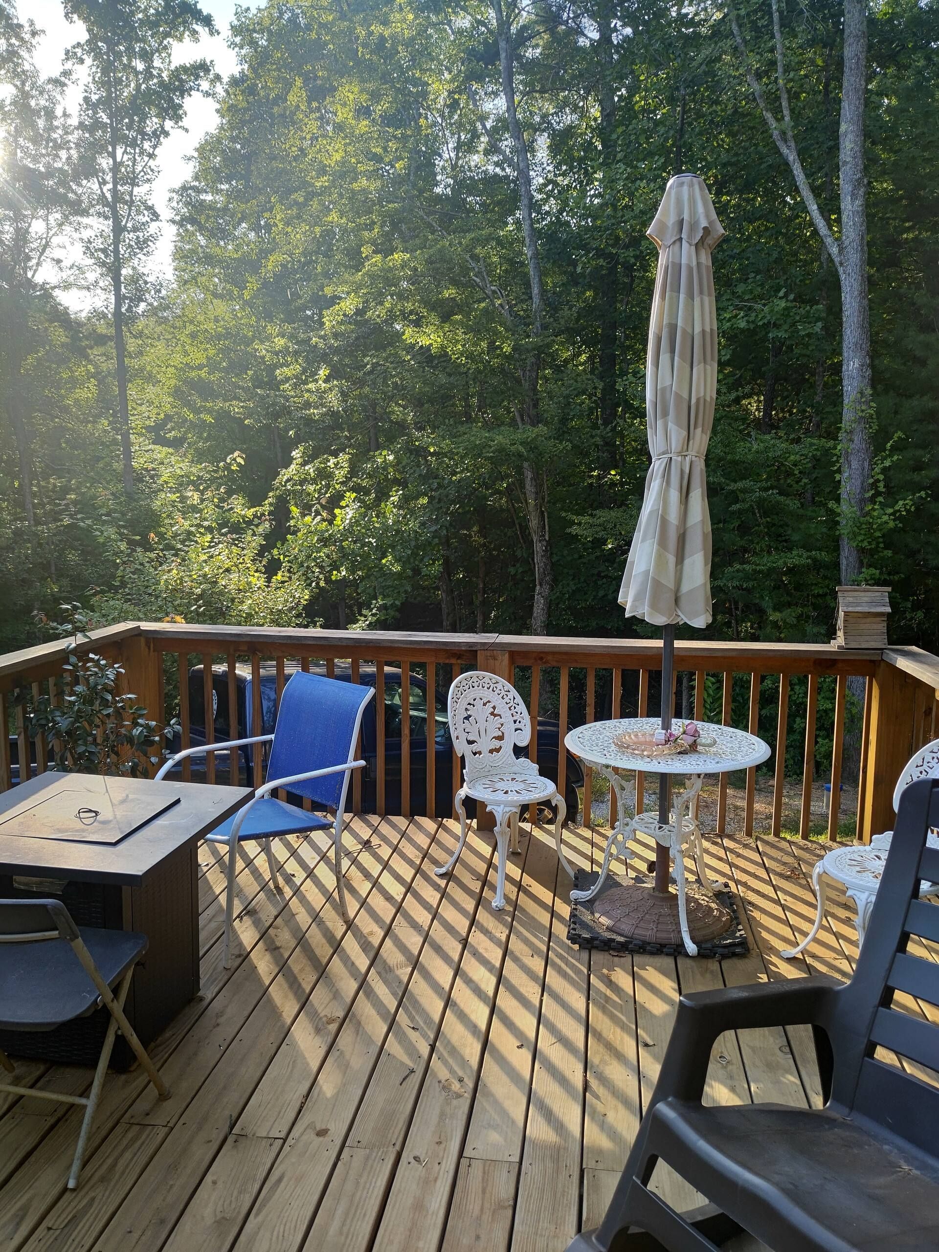 A wooden deck with outdoor furniture, including chairs and a table, surrounded by trees.