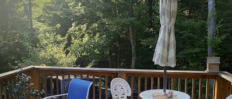 A wooden deck with outdoor furniture, including chairs and a table, surrounded by trees.