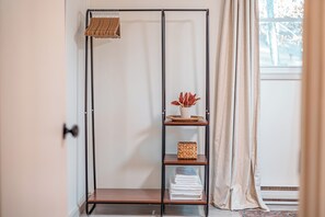 Ein Zimmer mit einem schwarzen Metallregal an der Wand, auf dem sich ein gewebter Korb, eine Vase mit roten Blumen und gefaltete Wäsche befinden.