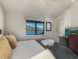 A bedroom with a bed, a window with a mountain view, a television, and a desk. - Peaceful Alpine Villa, Lake Views, Sleeps 6 (Queenstown)