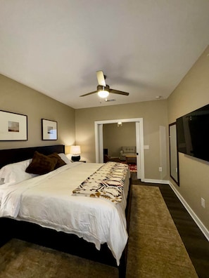 Une chambre à coucher comprenant un lit, un ventilateur de plafond, une table de chevet avec une lampe et une porte donnant sur une autre pièce.