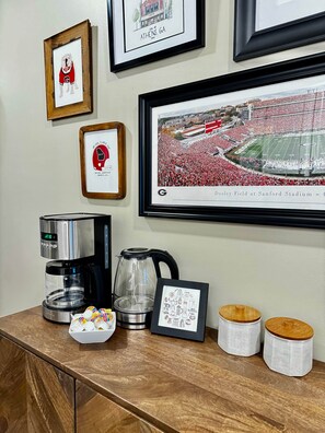 A coffee station with a coffee maker, a kettle, and a framed picture of a football stadium. - Pet Friendly Downtown Athens Condo W/ Parking (Athens)