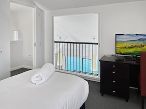 Ein Hotelzimmer mit einem Bett, einem Schreibtisch mit Fernseher, Blick auf einen Pool durch eine Balkontür und einem Schrank.