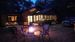 A cabin with a fire pit, outdoor seating, and a vehicle parked nearby.