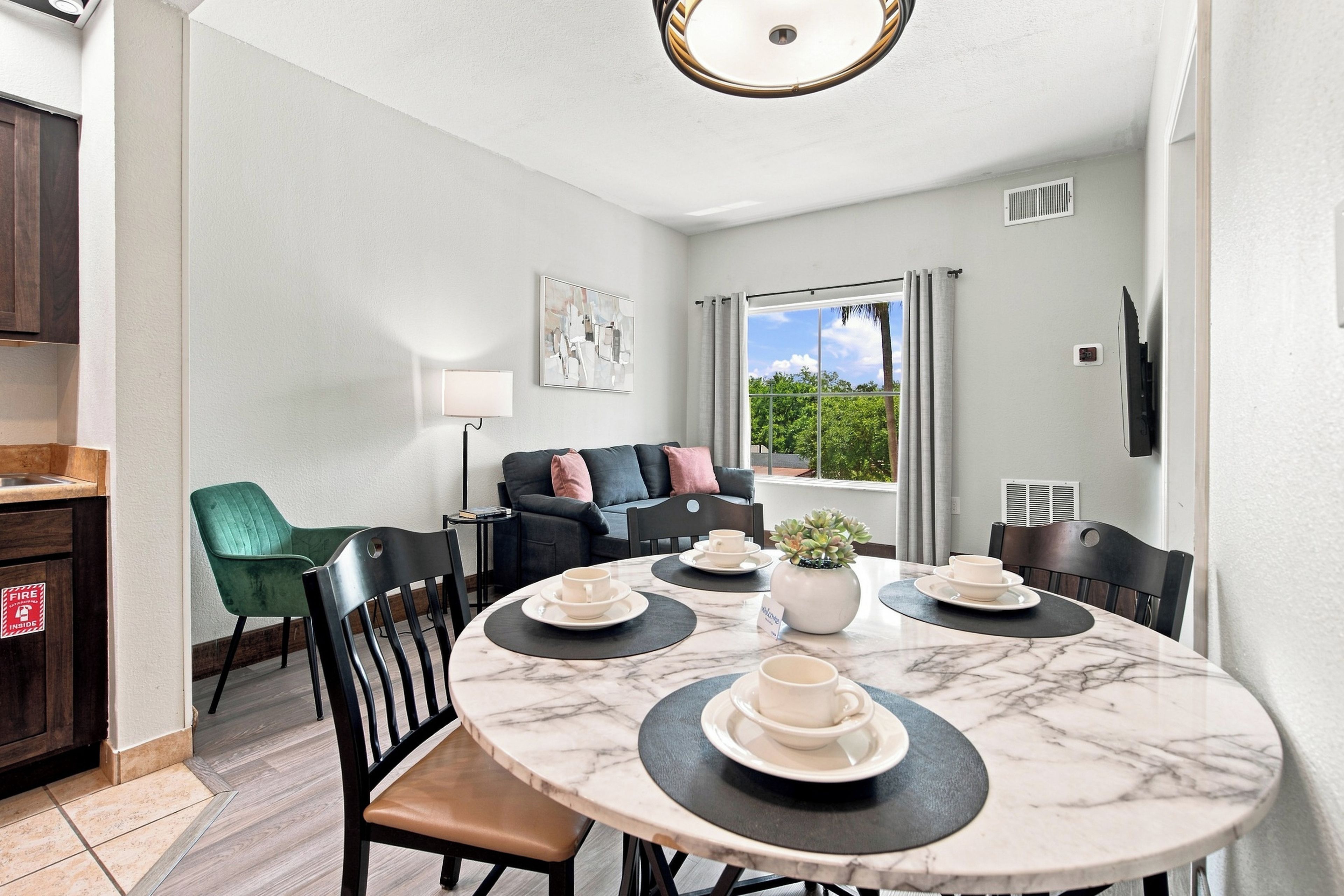 A modern kitchen with a dining area, a sofa, and a view of greenery outside.