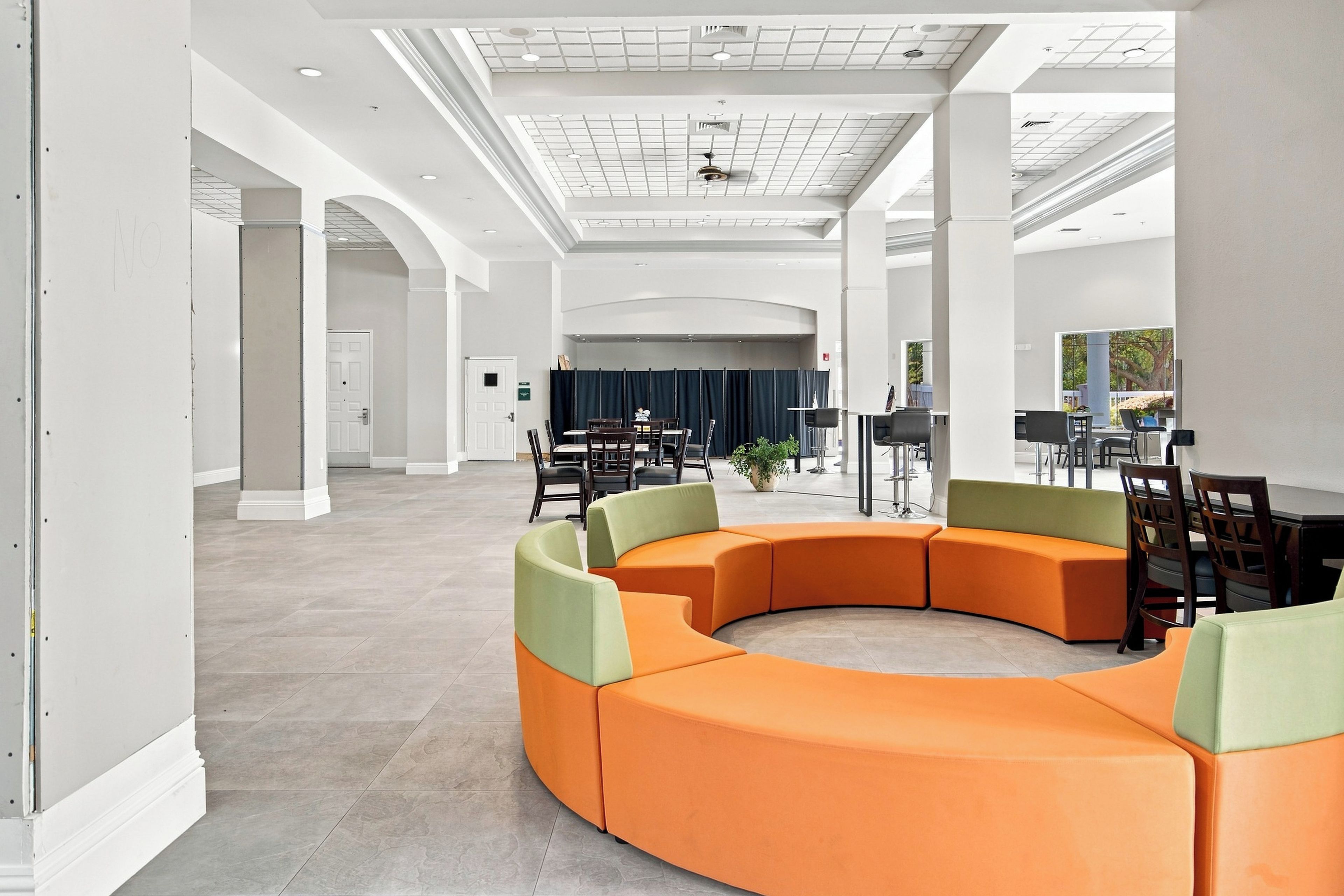 A spacious lobby with a curved orange seating area, a stage with curtains, and a large window offering a view of the outdoors.
