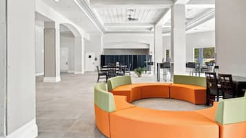 A spacious lobby with a curved orange seating area, a stage with curtains, and a large window offering a view of the outdoors.
