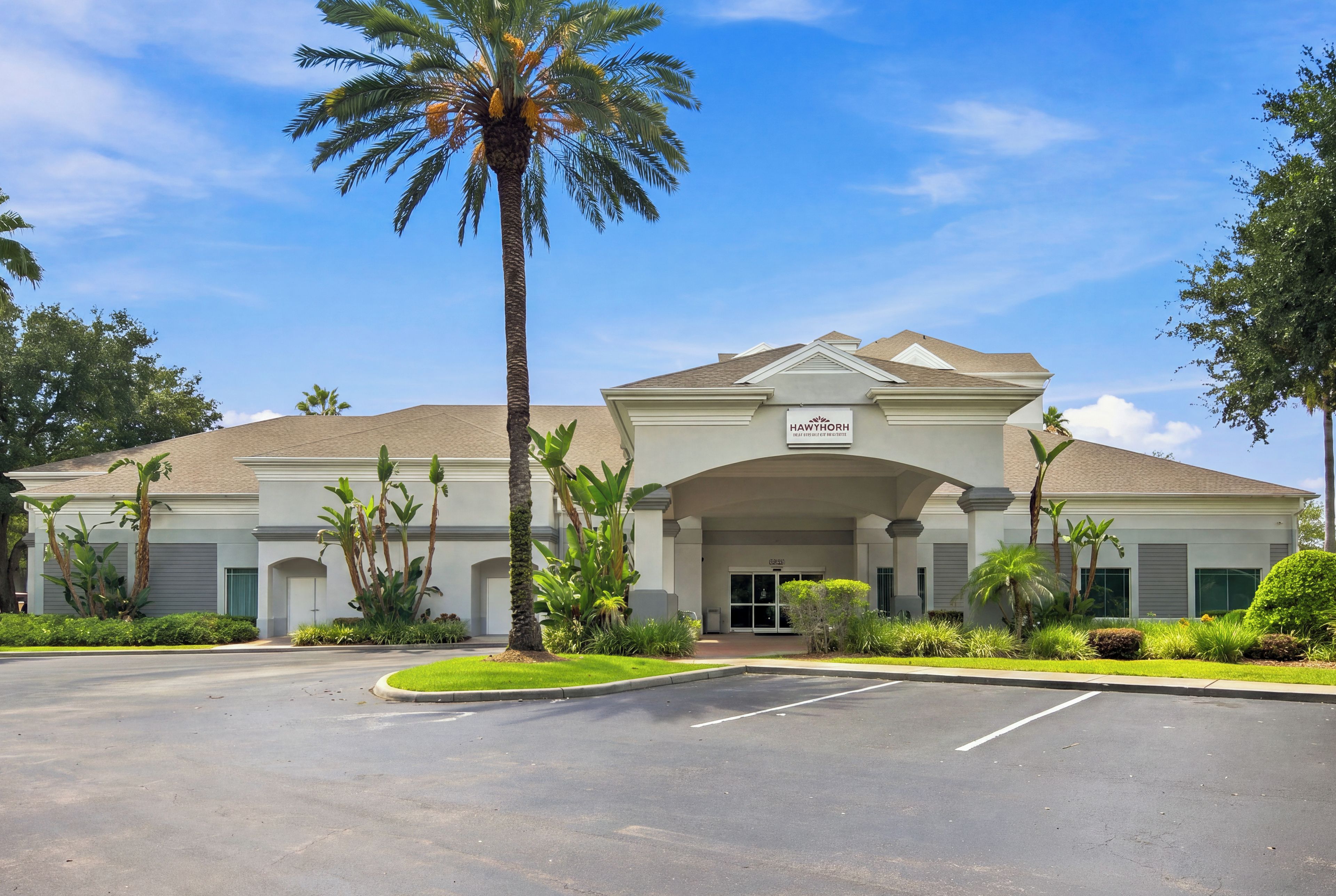 A hotel with a central entrance, palm trees, and a clear sky.