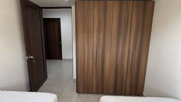 A hotel room with two beds, a wardrobe, and a ceiling fan.