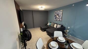 Una sala moderna con un sofá modular, una mesa de comedor preparada para cuatro personas y un ventilador de techo.