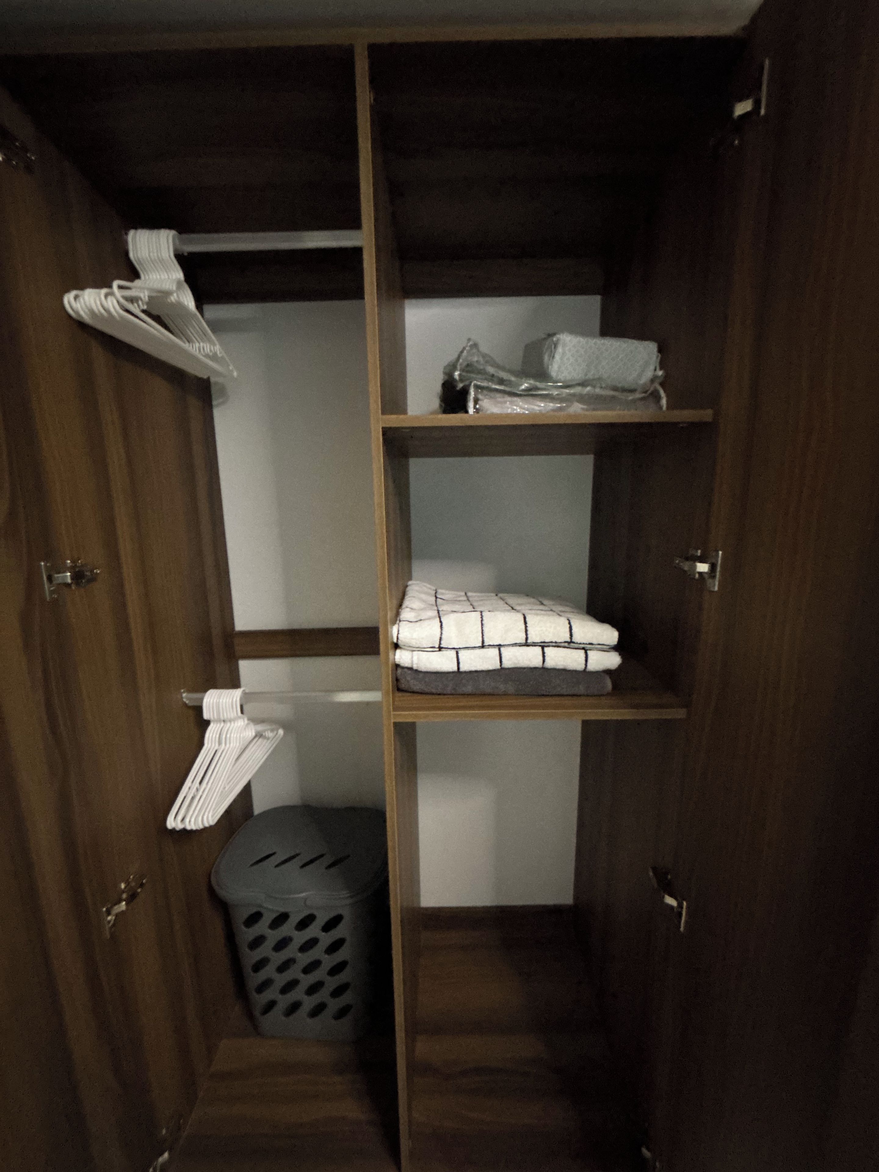 Un armario de madera con varios estantes, una barra para colgar ropa y un cesto de ropa.