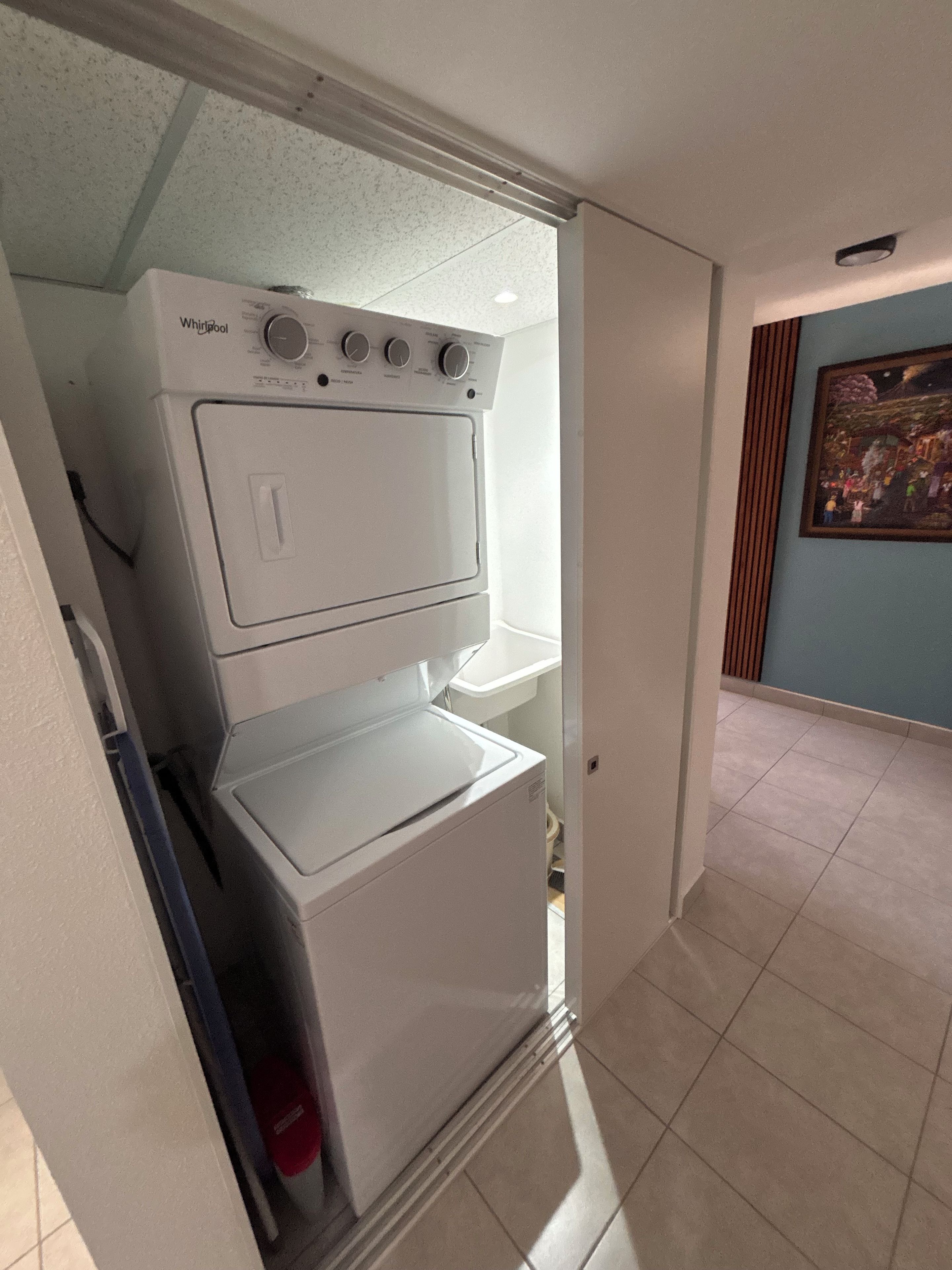 Un lavadero pequeño con lavadora y secadora Whirlpool, piso de baldosas y puerta que da a otra habitación.