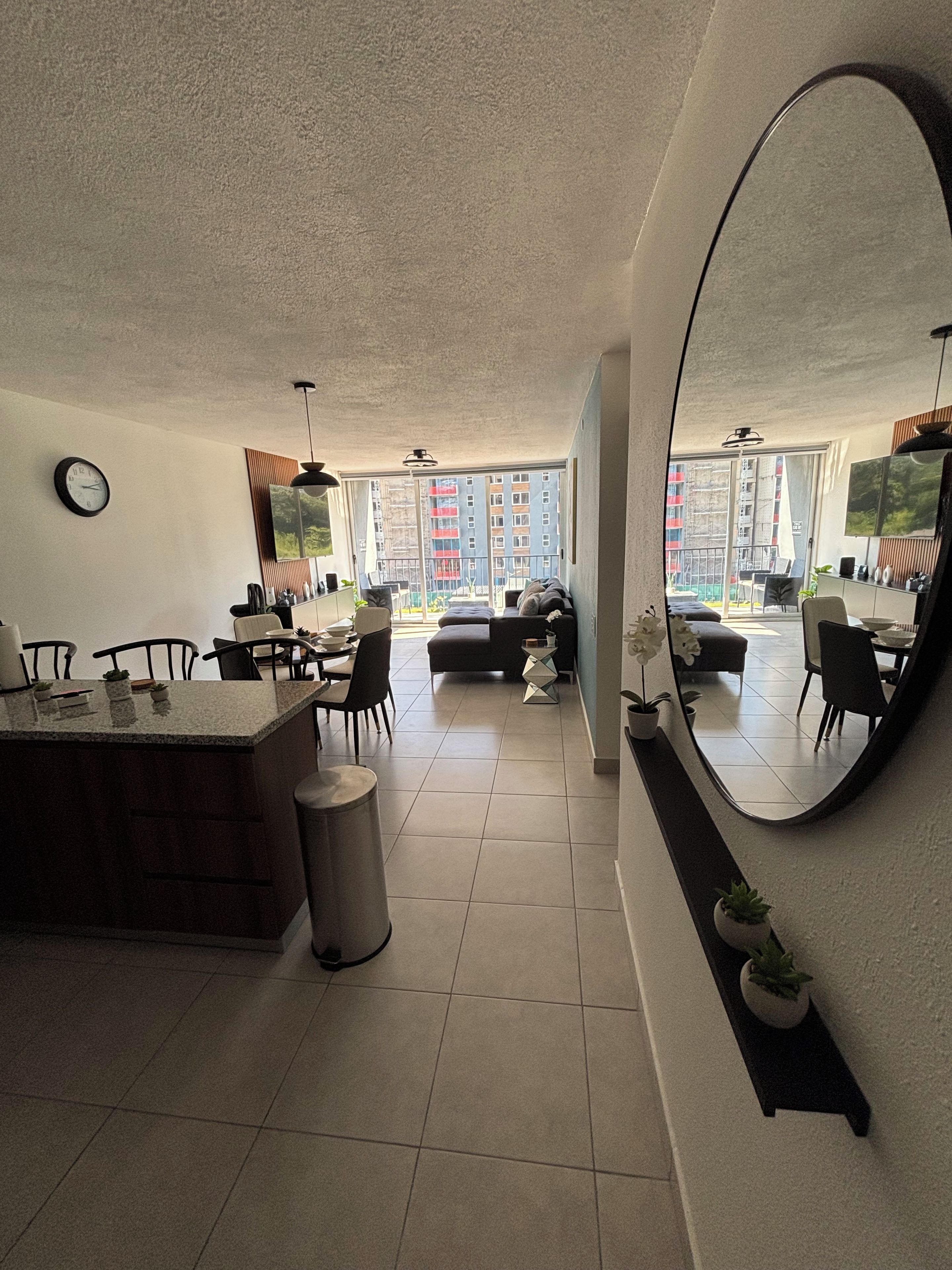 Une cuisine moderne avec un coin repas, de grandes fenêtres et une vue sur un immeuble d’habitation.