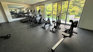 A gym with various exercise equipment, large windows, and a view of greenery outside.