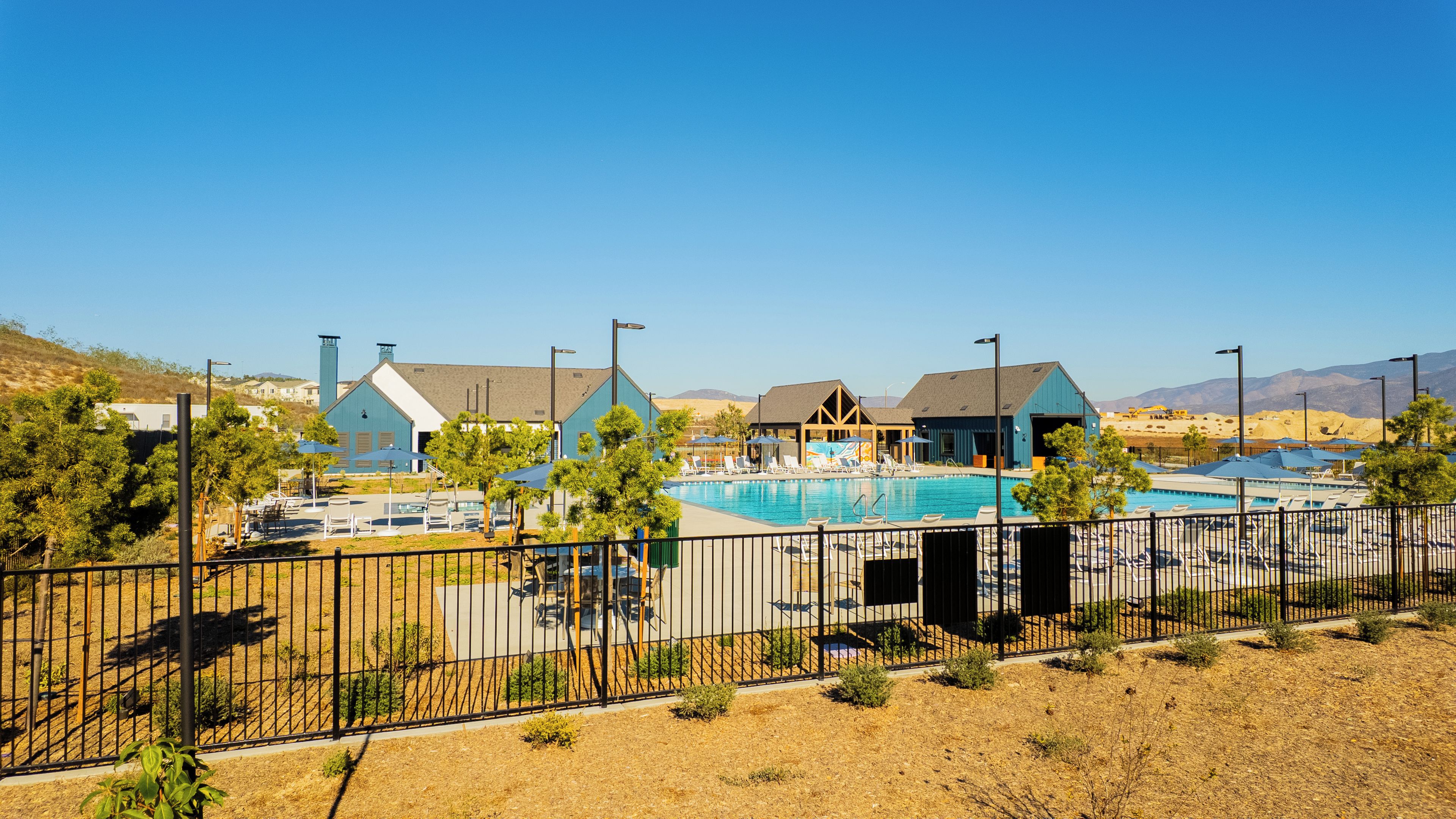 A pool area with lounge chairs and umbrellas, surrounded by a fence.