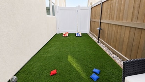 A backyard with artificial grass, a white fence, and a wooden fence.