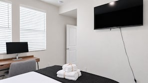 A hotel room with a bed, a desk with a computer, a TV mounted on the wall, and a door. - Private Modern Suite | Pool | Park (Chula Vista)